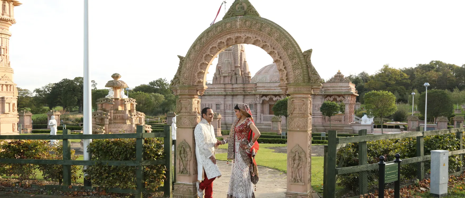 Bride and groom walking beneath a carved stone archway with domed buildings behind