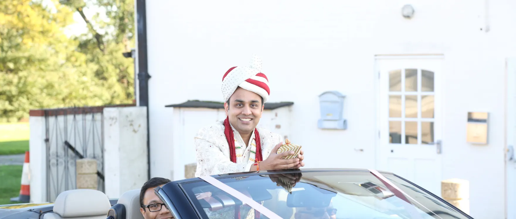 Groom in a cream sherwani and turban stepping out of an open-top car