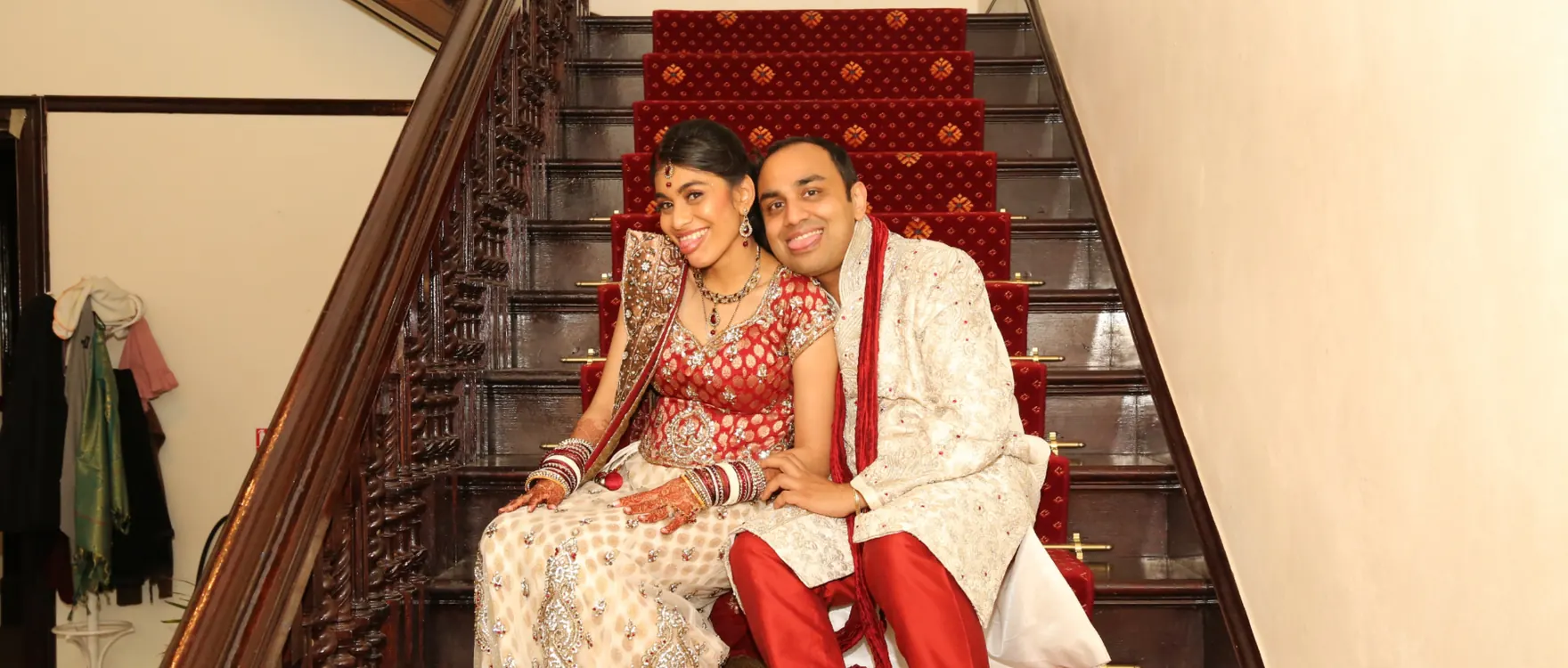 Bride and groom seated together on a wooden staircase in red and cream wedding dress