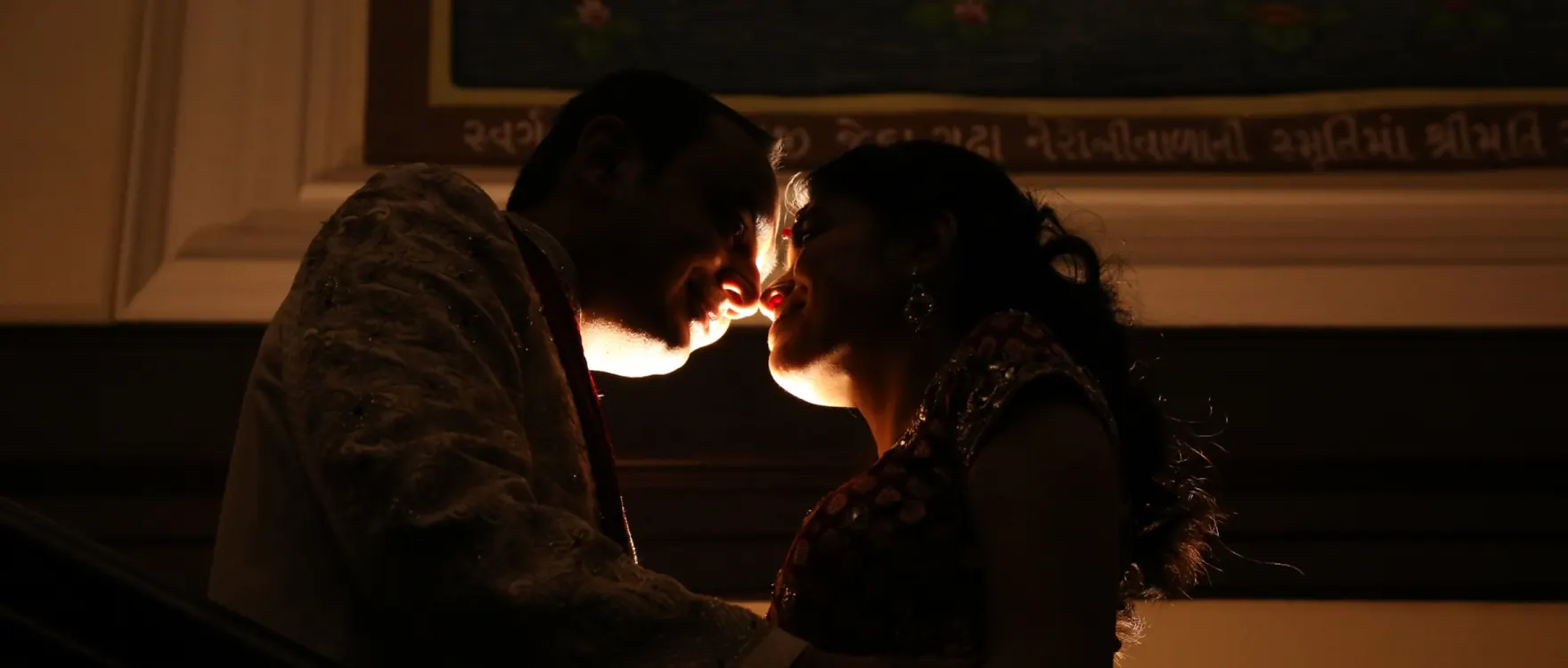 Bride and groom in profile, foreheads almost touching, backlit in a dark hall
