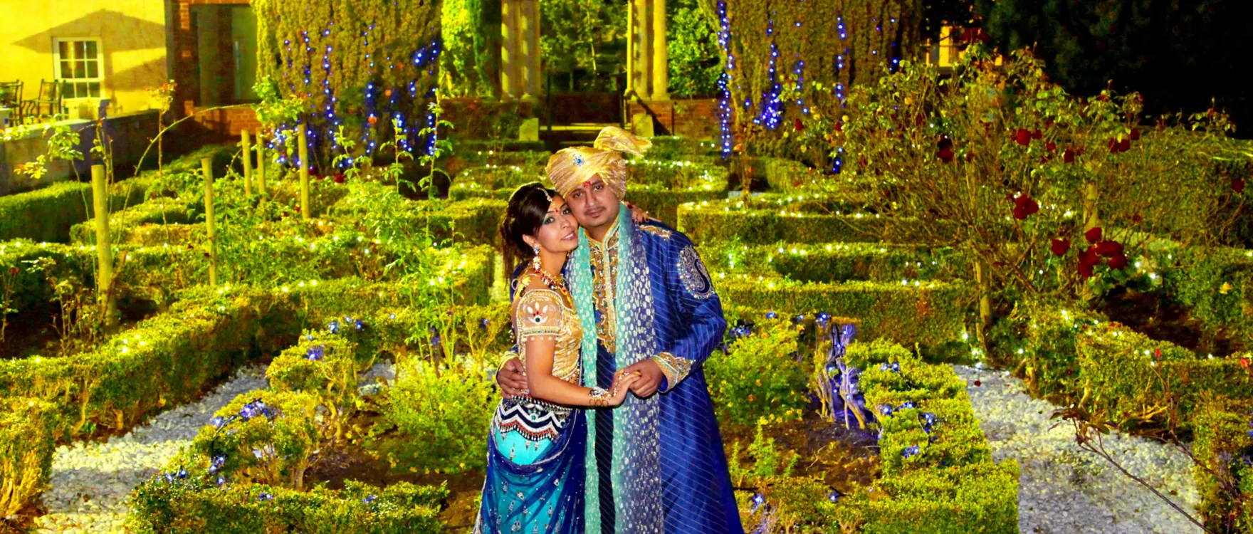 Bride in teal and groom in blue in a formal knot garden