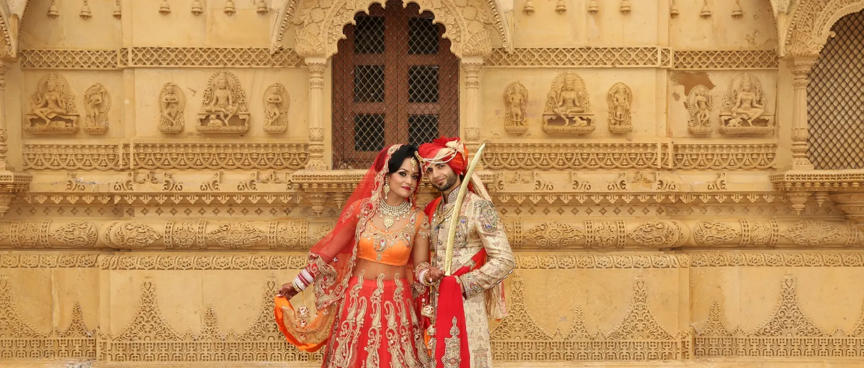 Bride in red and groom in a turban framed by carved stone arches