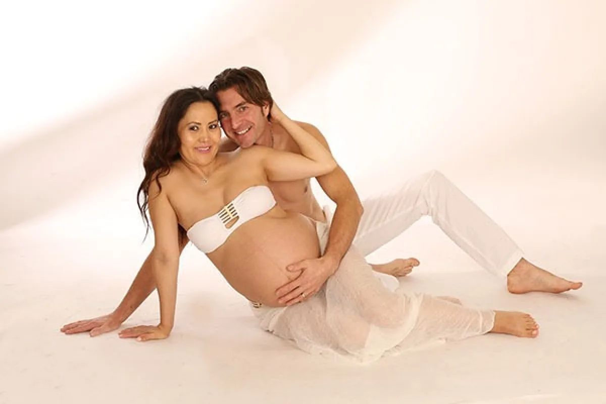 Expectant couple seated together on the studio floor, maternity portrait