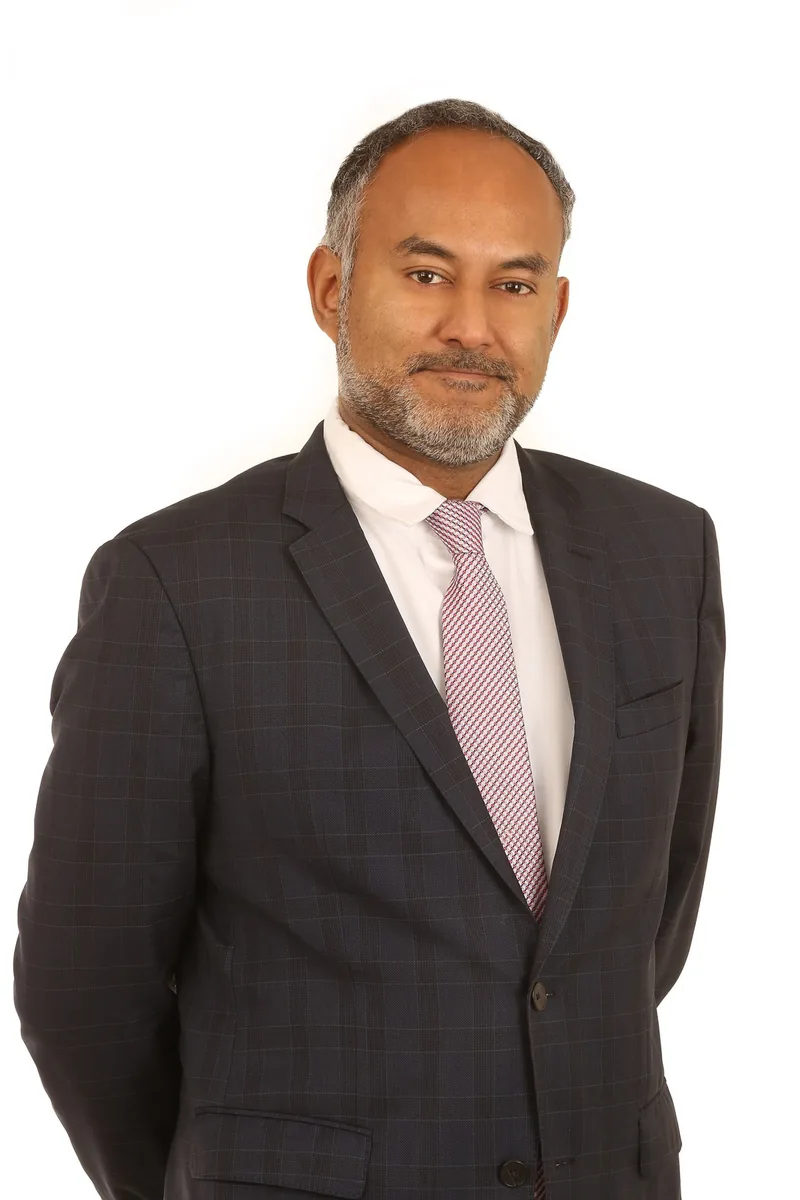 Studio headshot in a dark blazer on a light background