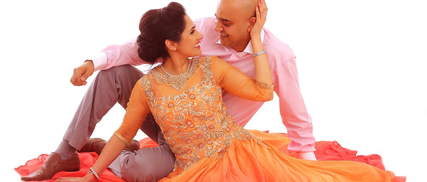 Couple seated on the studio floor, she in an orange gown