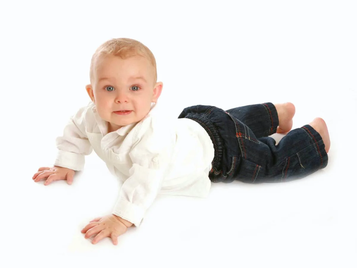 Baby in a white top and jeans crawling towards the camera in the studio