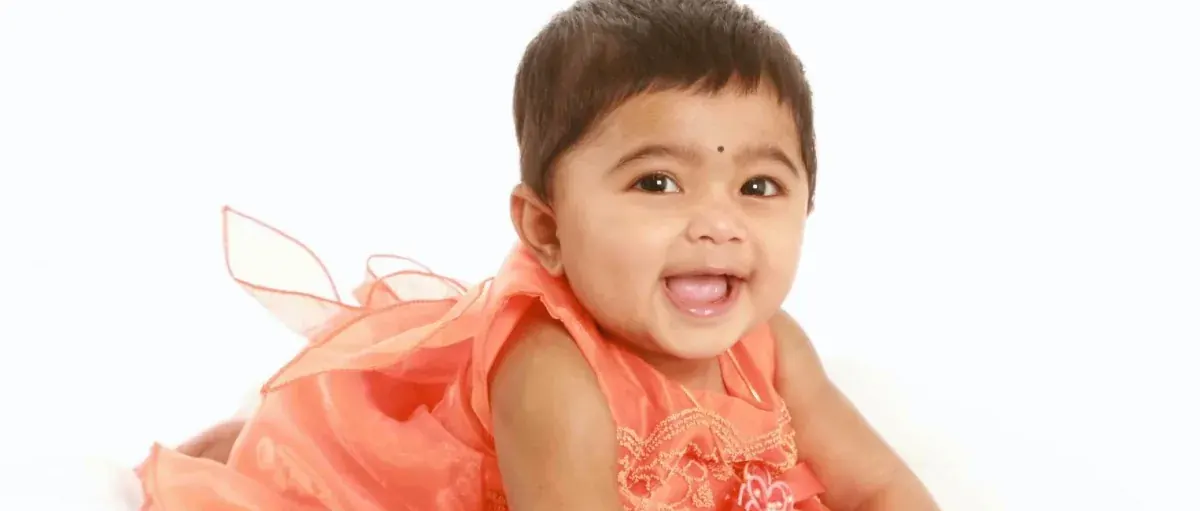 Smiling baby girl in a coral dress lying on her front in the studio