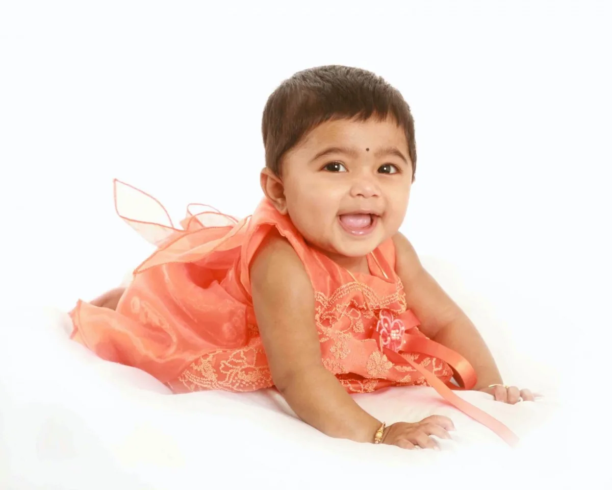 Smiling baby girl in a coral dress lying on her front in the studio